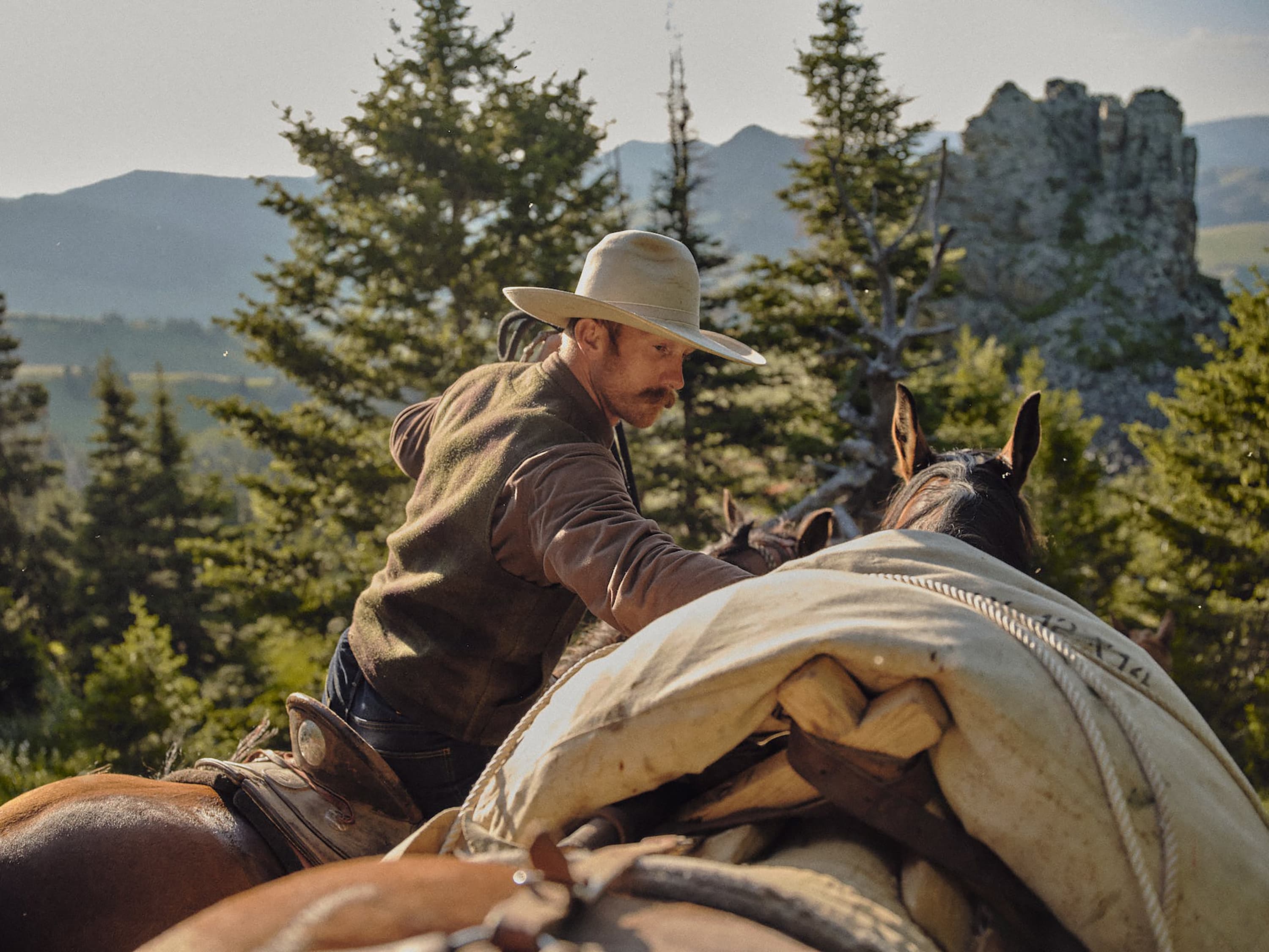 A frontiersman on horseback leading another horse through the great American West.